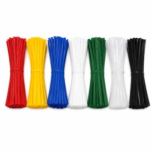 Op de afbeelding: Zeven bundels plastic bindstrips gerangschikt in een rij. De kleuren van links naar rechts zijn rood, geel, blauw, wit, groen, doorschijnend wit en zwart. Elke bundel is in het midden vastgezet met een bijpassende plastic bindstrip.