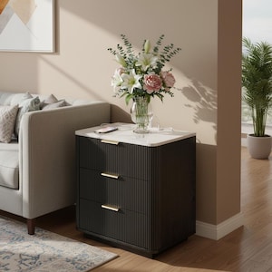 May include: A black nightstand with three drawers featuring vertical fluted detailing and slim gold-toned horizontal handles. The top surface is white and holds a clear glass vase filled with white lilies, pink peonies, and green eucalyptus.