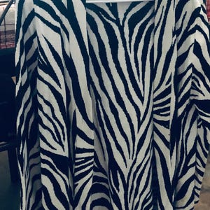 May include: A black and white zebra print cardigan with a long sleeve and a tie at the waist.