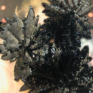 May include: Black sequined embellishments in the shape of leaves. The embellishments are made of small, round sequins that are sewn together to create a three-dimensional effect.
