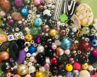 May include: A large assortment of colorful beads, including glass, plastic, wood, and metal. There are also some small charms and letters. The beads are in a clear plastic bag.