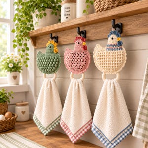 Puede incluir: Tres paños de cocina colgantes con figuras de pollo tejidas a ganchillo en verde, rosa y crema. Cada pollo está unido a un anillo de madera que sostiene una toalla crema texturizada con un borde de cuadros vichy en verde, rosa o azul.