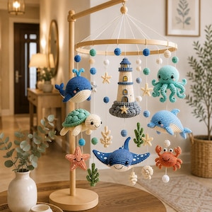 May include: A nautical-themed baby mobile featuring crocheted sea creatures including a blue whale, a green turtle, a light blue octopus, a dolphin, a stingray, and a crab, along with a central lighthouse, starfish, and coral accents.