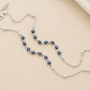 May include: A silver-toned chain anklet featuring a series of dark blue and white evil eye beads interspersed with small silver-toned metal spheres. The jewelry piece includes a lobster claw clasp and an adjustable extender chain at the end.