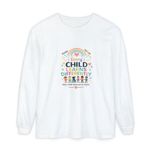 Peut inclure: Un t-shirt blanc à manches longues avec un motif coloré représentant un arc-en-ciel, des crayons et des enfants divers se tenant la main, dont un en fauteuil roulant. Le texte indique : Every CHILD LEARNS DIFFERENTLY Every Child Deserves to Shine.