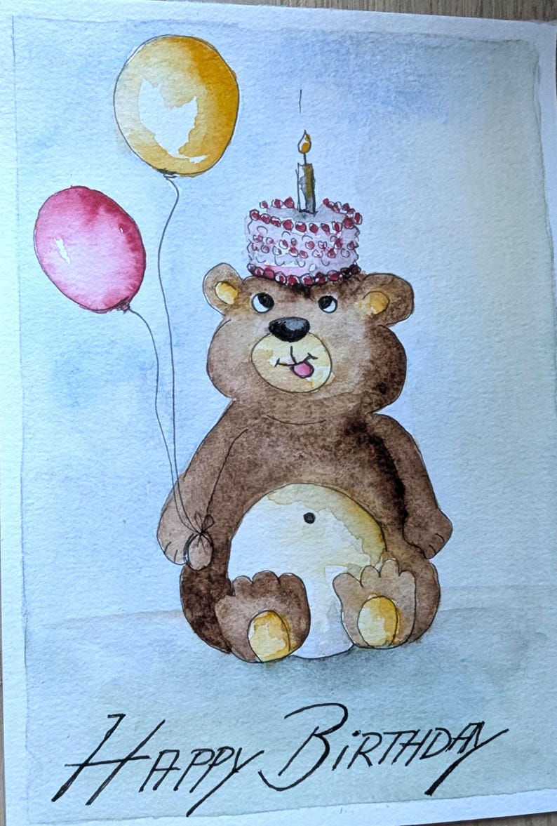 May include: A watercolor illustration of a brown bear with a light-colored belly, holding a yellow balloon and a red balloon. The bear has a small cake with a lit candle on its head and the text Happy Birthday written in black ink at the bottom.