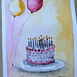 May include: A watercolor painting on paper featuring a white birthday cake with pink frosting details and numerous lit candles on a plate. Two balloons, one yellow and one dark pink, float above. The text Happy Birthday is written below.