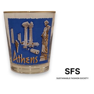May include: A clear glass tumbler featuring a blue rectangular graphic with white illustrations of ancient Greek columns, a torch, and a statue. The word Athens is printed in gold lettering at the bottom of the blue graphic, and the rim is gold.