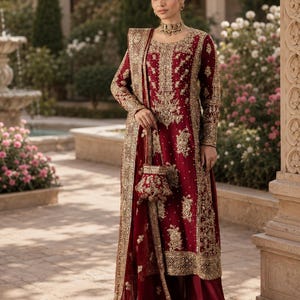 May include: A deep red long-sleeved tunic and wide-leg trousers set featuring intricate gold embroidery, beadwork, and sequins. The ensemble includes a matching sheer dupatta with a gold-embroidered border and a small, matching embellished handbag.