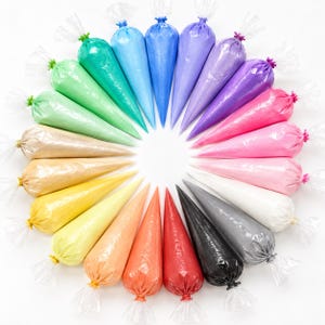May include: A circular arrangement of nineteen clear plastic piping bags filled with icing in a spectrum of colors including green, blue, purple, pink, white, black, gray, red, orange, yellow, gold, and beige, each tied at the top with a small tie.