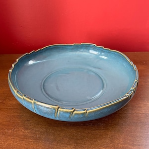 May include: A blue ceramic bowl with a textured, uneven rim and a gold-colored glaze. The bowl is sitting on a wooden surface.