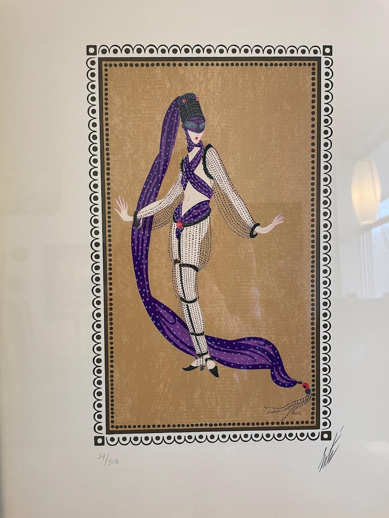 May include: A framed print of a woman in a purple and black costume with a mask. The woman is standing in a gold frame with a black and white border. The print is numbered 34/308.