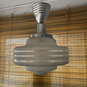 May include: A pendant light fixture featuring a tiered, frosted glass shade with horizontal clear glass bands. The fixture includes a brushed metal top cap and a matching ribbed, conical ceiling canopy, suspended by a single white cord.