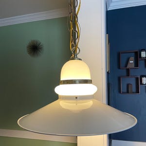 May include: A white ceiling light fixture with a round, frosted glass shade and a wide, flat, white metal base. The light is hanging from a chain.