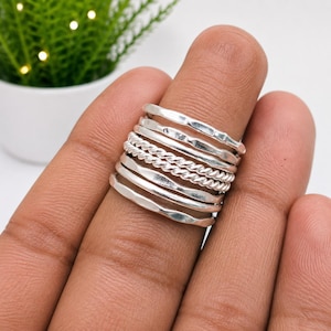 May include: A stack of five silver rings worn on a finger. The set includes three rings with a smooth, slightly hammered finish and two rings featuring a twisted, rope-like texture. The rings are arranged in an alternating pattern of smooth and twisted bands.