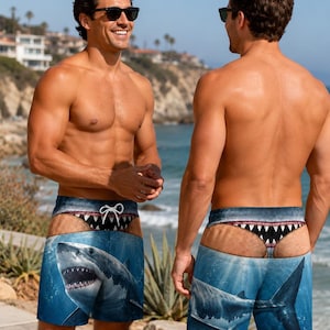 May include: Blue swim trunks featuring a realistic graphic print of a great white shark swimming underwater. The waistband area displays a printed design of a shark's open mouth with sharp teeth, creating a visual illusion of a thong underneath.