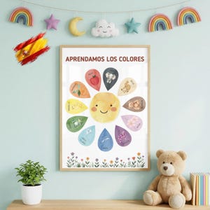 May include: A framed educational wall poster titled APRENDAMOS LOS COLORES featuring a central yellow sun surrounded by colorful teardrop shapes, each containing a small illustration and a Spanish color name, with floral graphics at the bottom.