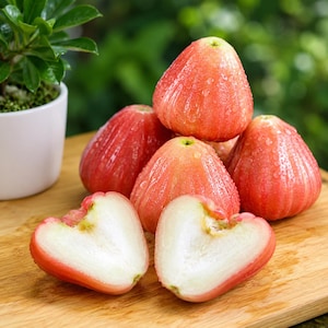 May include: A cluster of bell-shaped wax apples with smooth, glossy, pinkish-red skin and water droplets on the surface. Two of the fruits are sliced in half, revealing a crisp, pale white interior flesh with a hollow center and a light green core.
