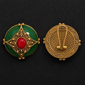 May include: A pair of round clip-on earrings featuring a dark green circular base with an ornate gold-toned metal overlay. The centre of each earring is set with a smooth, oval-shaped red stone. The back shows a textured gold metal clip mechanism.