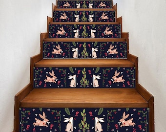 May include: Wooden staircase with decorative stair treads featuring a navy blue background. The treads are adorned with a repeating pattern of white and pink rabbits, green leaves, and red berries, creating a whimsical and nature-inspired design.