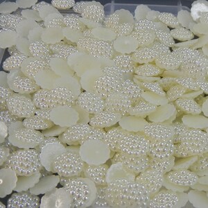 May include: A large quantity of white pearl embellishments. Each embellishment is a flat, round disc with a raised center covered in small white pearls.