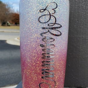 Op de afbeelding: Een roze en witte ombre glitterbeker met een zwarte cursieve inscriptie die "Be Amazing" leest.