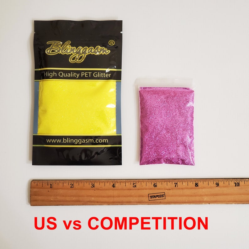 Op de afbeelding: Twee kleine zakjes glitter, een gele en een roze, worden naast een liniaal getoond. De zakjes zijn gelabeld met "Blinggasm High Quality PET Glitter" en "www.blinggasm.com". De tekst "US vs COMPETITION" staat onder de liniaal.