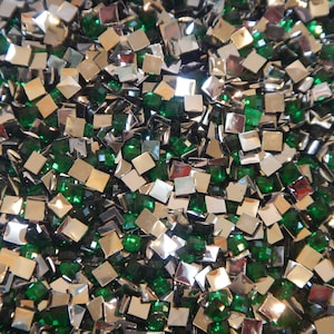 May include: A close-up image of a large quantity of small, square-shaped rhinestones. The rhinestones are a mix of silver and green.