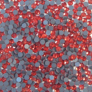 May include: A close-up image of a large quantity of red rhinestones. The rhinestones are arranged in a random pattern and are surrounded by gray adhesive backing.