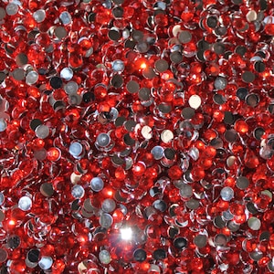 May include: A close-up image of a large quantity of red and silver round rhinestones. The rhinestones are scattered randomly and appear to be made of glass or plastic.