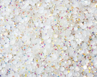 May include: A close-up image of a large quantity of iridescent white rhinestones. The rhinestones are small and round, and they are scattered randomly across the surface.