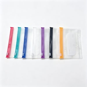 May include: A set of seven translucent plastic pouches with colored zipper seals in pink, teal, blue, white, purple, black, and orange. Each pouch features the text PILL POUCH printed in white, along with a designated area for Name and Day.