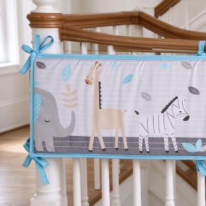 May include: A rectangular crib bumper pad featuring a light gray background with thin white horizontal stripes. The fabric displays a printed pattern of a gray elephant, a tan giraffe, and a black and white zebra, accented with blue and gray leaves.