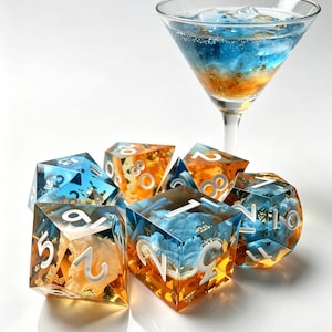 Pode incluir: Um conjunto de dados poliédricos feitos de resina translúcida com um gradiente de azul e laranja, flocos de ouro incrustados e números brancos, posicionados em frente a uma taça de martini com um líquido azul e laranja em camadas.