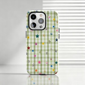 Puede incluir: Una funda para smartphone con un patrón de cuadros vichy en verde claro y blanco, decorada con pequeñas estrellas multicolores en varios tonos como amarillo, azul, rosa, rojo y plata, con un recorte negro para la cámara en la parte superior.