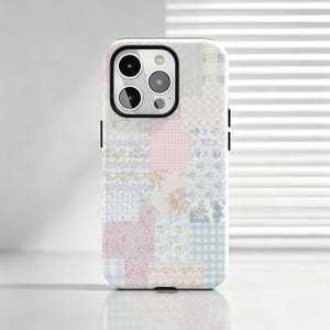 Könnte beinhalten: Eine Smartphone-Hülle mit einem Patchwork-Design aus verschiedenen hellen Mustern, darunter rosa und blaues Vichy-Karo, kleine Blumenmuster und Toile-Motive. Die Hülle hat einen schwarzen Ausschnitt für das Kameramodul oben links auf der Rückseite.
