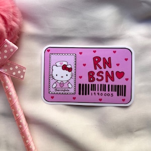 Puede incluir: Pegatina rosa y blanca con un dibujo animado de Hello Kitty vestida de enfermera. La pegatina dice "RN BSN" con un coraz&oacute;n y un c&oacute;digo de barras que dice "1990005".