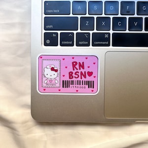 Puede incluir: Pegatina rosa con una ilustraci&oacute;n de Hello Kitty vestida de enfermera. La pegatina dice "RN BSN" con un s&iacute;mbolo de coraz&oacute;n y un c&oacute;digo de barras con el n&uacute;mero "1990005".