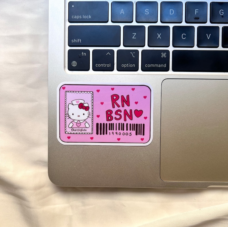Puede incluir: Pegatina rosa con una ilustraci&oacute;n de Hello Kitty vestida de enfermera. La pegatina dice "RN BSN" con un s&iacute;mbolo de coraz&oacute;n y un c&oacute;digo de barras con el n&uacute;mero "1990005".