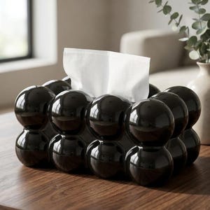 May include: A rectangular tissue box cover featuring a glossy black finish and a three-dimensional bubble-like texture composed of multiple interconnected spheres. A white tissue is pulled through the central opening at the top of the container.