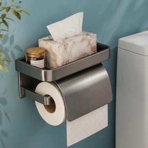 May include: A dark grey metal wall-mounted bathroom organiser featuring a top shelf for a marble-patterned tissue box and a small glass jar, with an integrated lower dispenser bar holding a roll of white toilet paper with a diamond pattern.