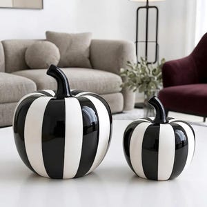 Può includere: Due zucche decorative con finitura lucida, caratterizzate da strisce verticali alternate bianche e nere. Ogni zucca ha un corpo liscio e curvo con un gambo nero solido sulla parte superiore, presentate come una coppia di dimensioni diverse.