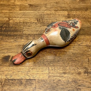 May include: Hand-painted ceramic bird-shaped figurine. The beige body features a red bird and black leaf design. The beak and neck have red and black accents. A unique decorative piece.
