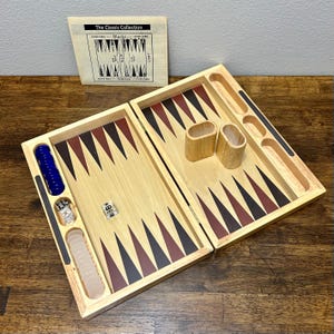 Puede incluir: Una taza de cerámica blanca con un asa negra y el texto "But First, Coffee" en negrita negra. La taza se encuentra sobre un fondo neutro, resaltando su diseño simple.