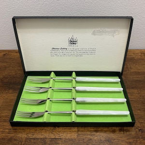 Könnte beinhalten: Ein Set aus vier Chateau Cutlery Gabeln in einer schwarzen Box mit grünem Innenraum. Die Gabeln haben Edelstahlzinken und weiße Griffe. Auf der Box steht "Chateau Cutlery France".