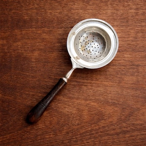 Puede incluir: Una taza de cerámica blanca con un asa negra y el texto "But First, Coffee" en negrita negra. La taza está sobre una superficie blanca. La taza mide aproximadamente 10 cm de alto.