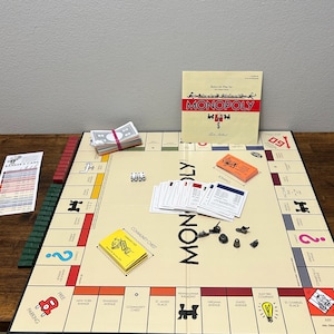 May include: A Monopoly board game set with a beige game board, cards, dice, play money, and game pieces. The game board features property spaces, community chest, and chance cards. The game box is visible in the background.