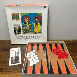 May include: A Pressman Backgammon board game set featuring a square box with an illustration of two figures, a game board with orange and black triangles, white and red playing pieces, two white dice, and an instruction booklet with a photo.