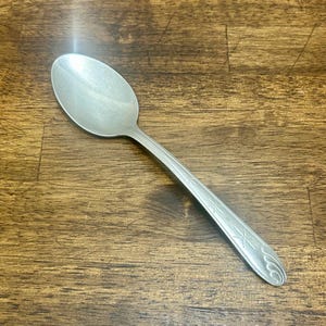 Op de afbeelding: Een zilveren lepel met een afgeronde kom en een lange steel. De steel is versierd met stervormige ontwerpen en gebogen lijnen. De lepel is gemaakt van een glanzend, metalen materiaal.