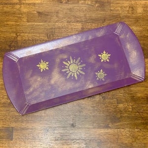 May include: A rectangular purple tray with rounded corners and gold accents. The tray features a gold sun and star design. The tray is made of wood and has a distressed finish.